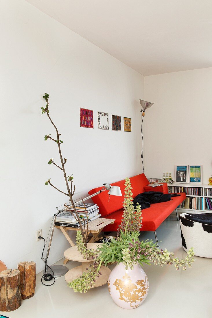 Bodenvase mit Blumenzweigen, rotes Designersofa und Hocker mit Kuhfellbezug, in minimalistischem Wohnraum