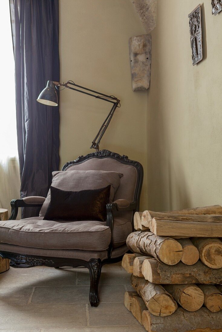 Rococo-style armchair and standard lamp in corner next to stack of firewood against wall