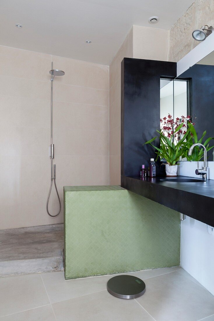 Dunkle Waschtischzeile und grüne Brüstungswand vor schlichtem Duschbereich