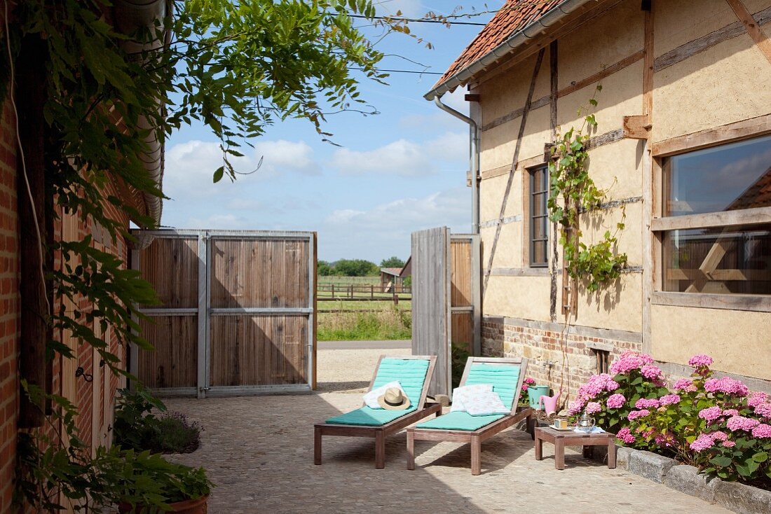 Sonnenliegen und blühende Hortensien in gepflastertem Innenhof eines renovierten Bauernhofes