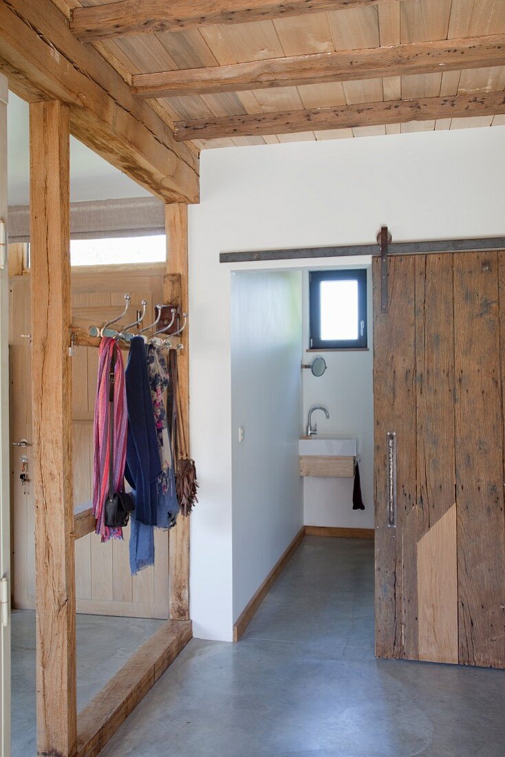 Timber-framed cloakroom area with view into toilet through rustic vintage sliding door