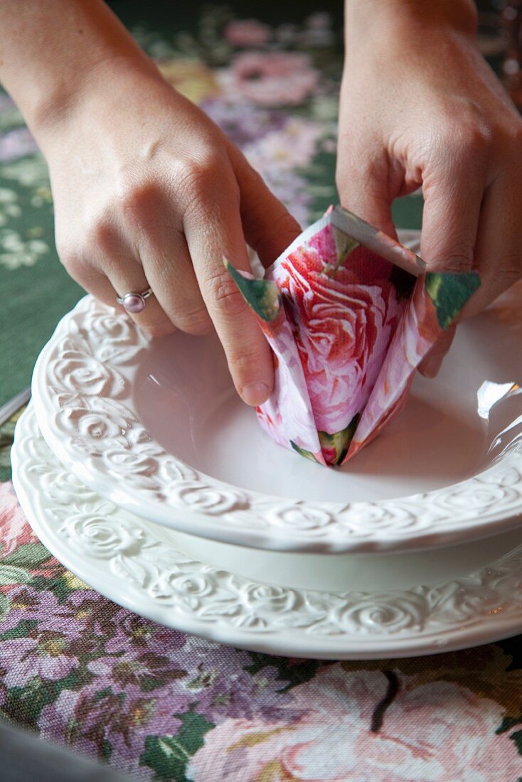 Hand hält gefaltete Serviette mit Blumenmuster auf weißem Gedeck mit Prägemuster