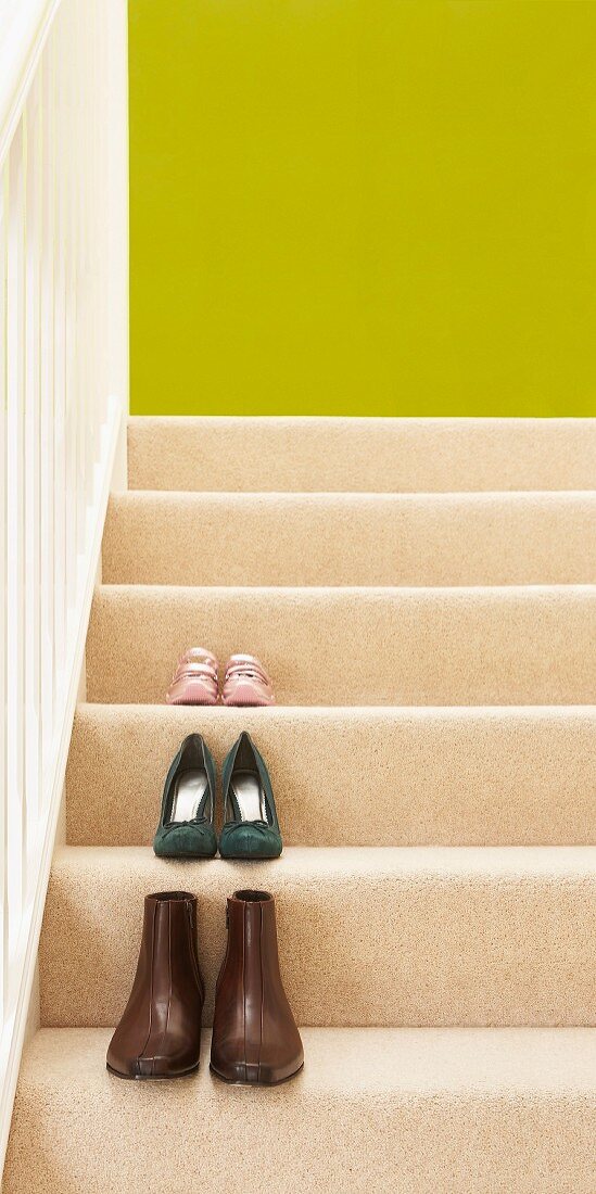 Schuhpaare auf den mit cremefarbenem Teppich belegten Stufen einer Holztreppe vor frühlingsgrünem Hintergrund