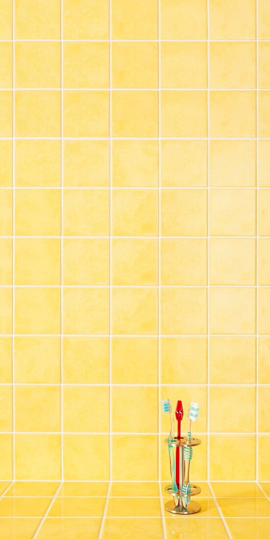 Zahnbürstenständer auf gelb gefliester Badezimmer-Ablage