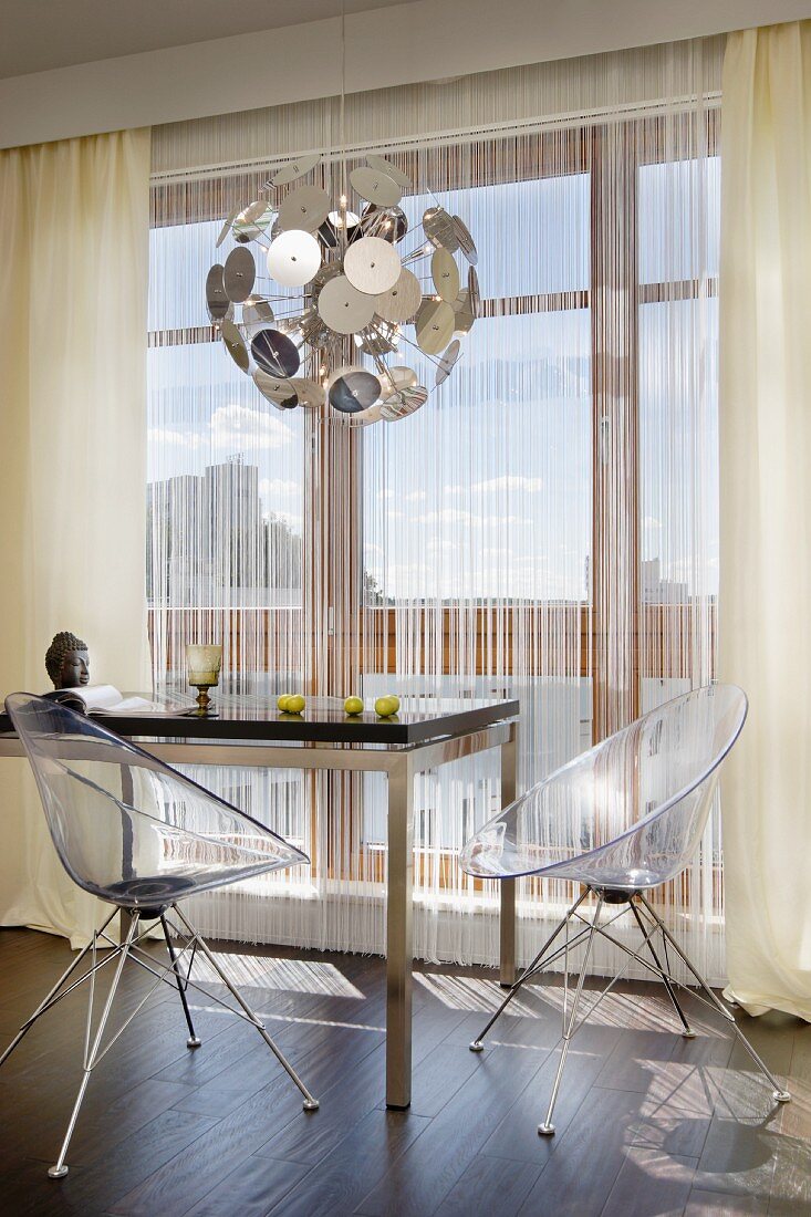 Schalensitze aus klaren Acrylglas an modernem Esstisch und Leuchtenklassiker Dandelion vor Fensterfront mit Schnurvorhang