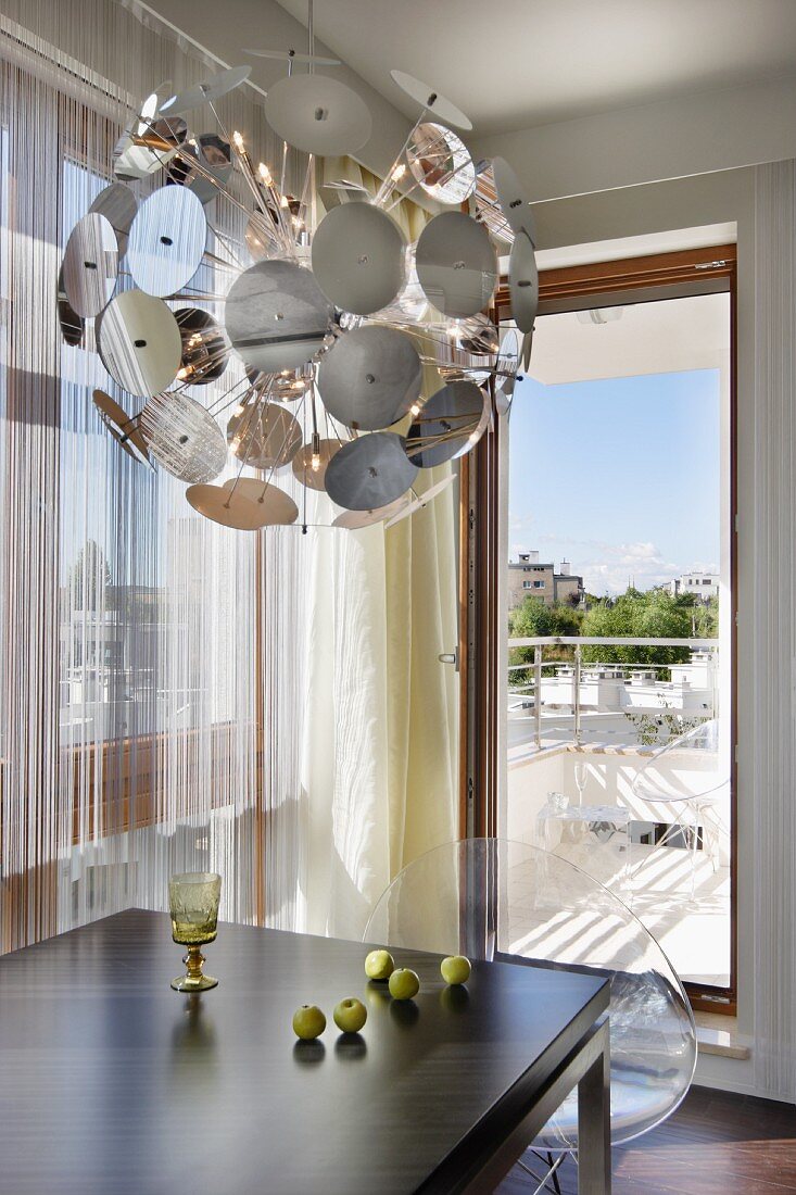Schalensitze aus klaren Acrylglas an modernem Esstisch und Leuchtenklassiker Dandelion vor Fensterfront mit Blick auf den Balkon