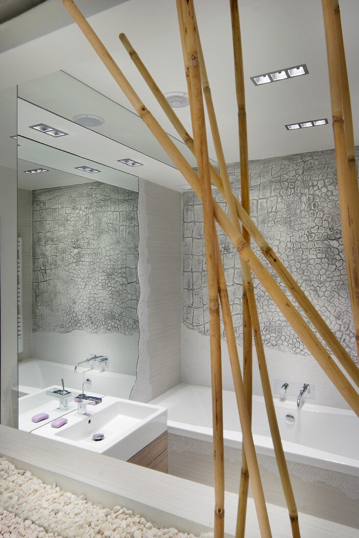 Reflektierende Spiegelflächen in künstlerisch gestaltetem Badezimmer; Elefantenhaut-Struktur über der Wanne, Bambusstreben im Vordergrund