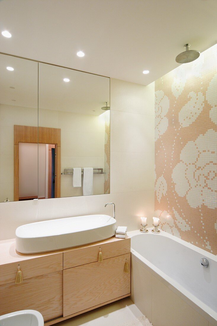 Floral tiled mosaic above bathtub and washstand with oval sink and tassels on drawers