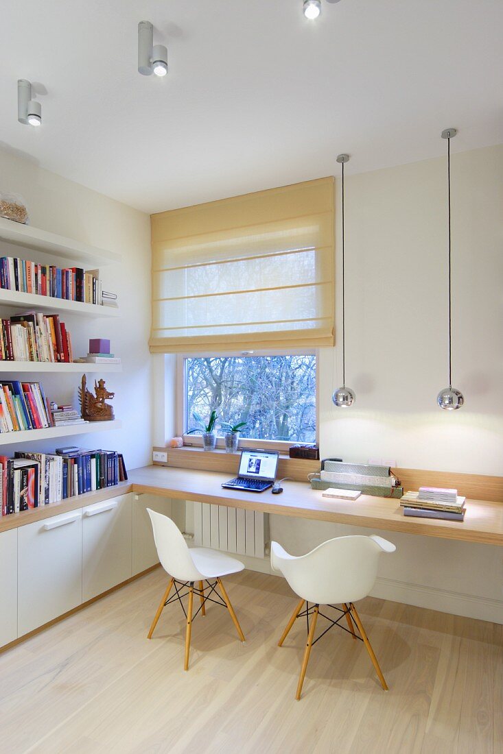 Spherical chrome lamps above narrow desk and Eames chairs with bookshelves to one side and Roman blind on window
