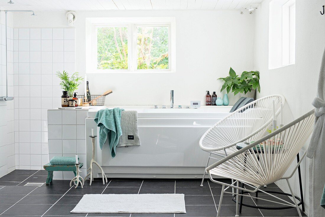 White, retro cord chairs next to bathtub below window and open shower area in modern, white bathroom