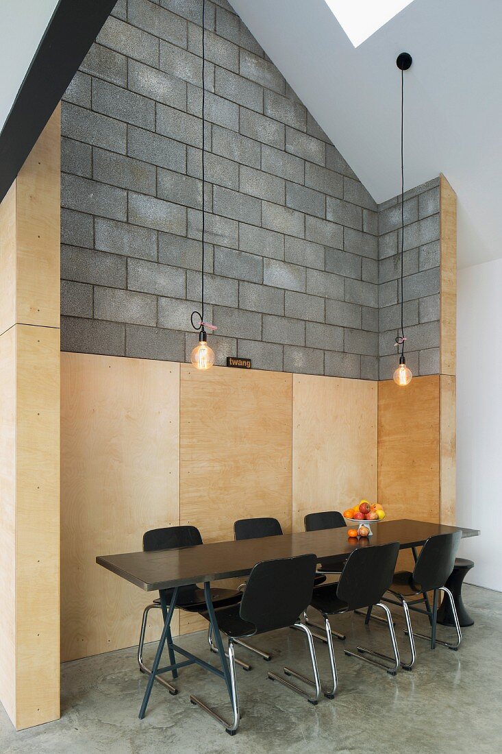 Schwarze Holzschalenstühle um Tisch im Retro Stil vor abgesetzten Wandpaneelen aus Holz und Betonsteinmauer