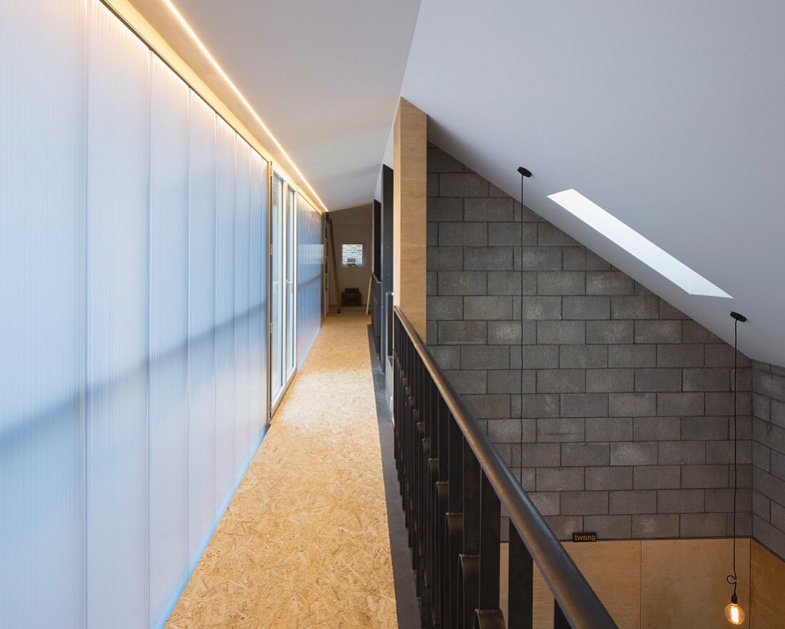 Narrow gallery with metal balustrade and frosted glass wall; open-plan, double-height interior with sloping ceiling to one side