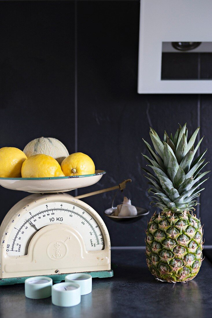 Auf Vintage Küchenwaage Zitronen und Melone, seitlich Ananas, auf dunkelgrauer Ablage