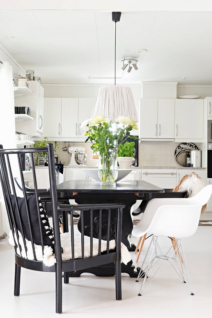 Armchair with black-painted wooden frame and white shell chair at table in open-plan, fitted kitchen