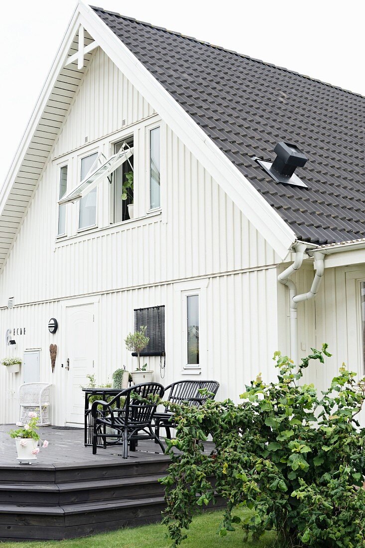House with white-painted wooden façade and outdoor furniture on raised wooden deck