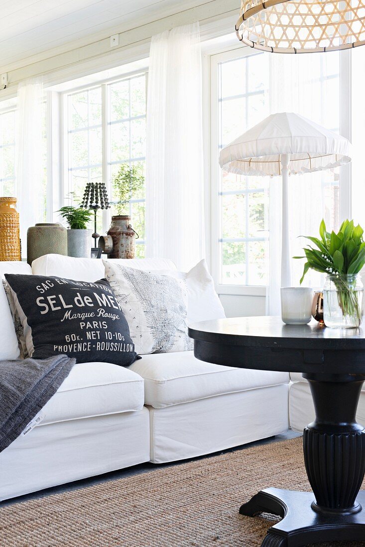 Black round table and white sofa with scatter cushions in front of standard lamp with white fabric lampshade