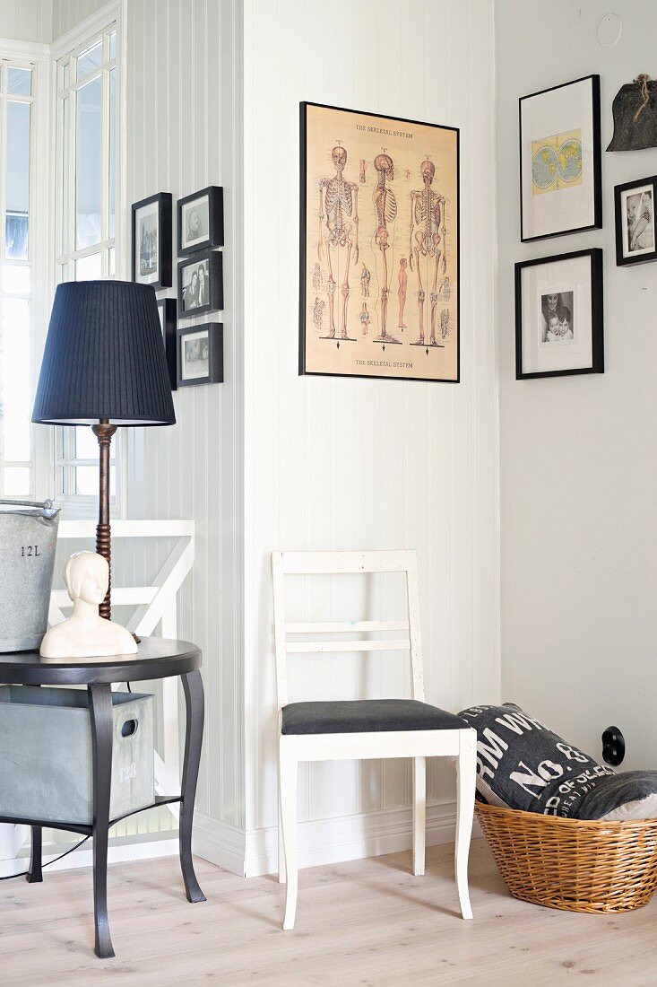 White-painted chair with black seat cushion below framed pictures in corner