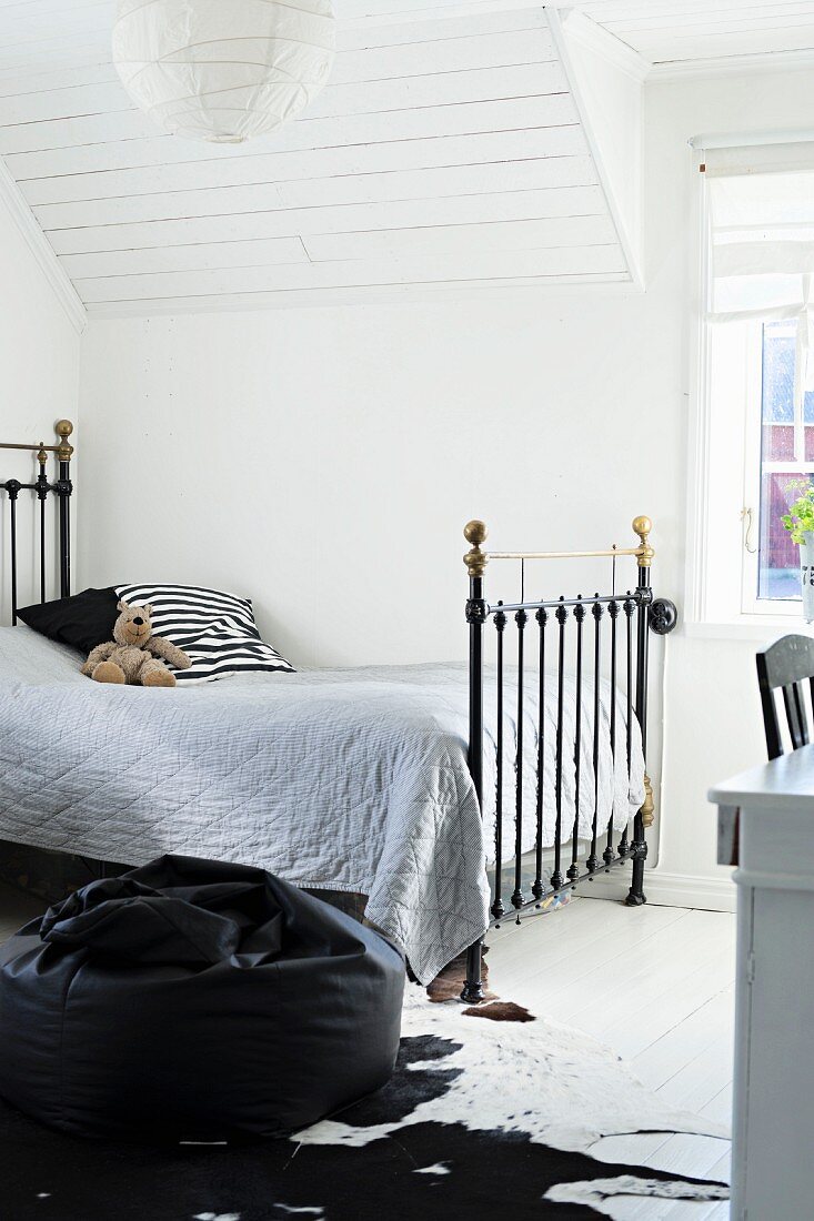 Vintage metal bed with grey bedspread in attic room with white, wood-clad sloping ceiling
