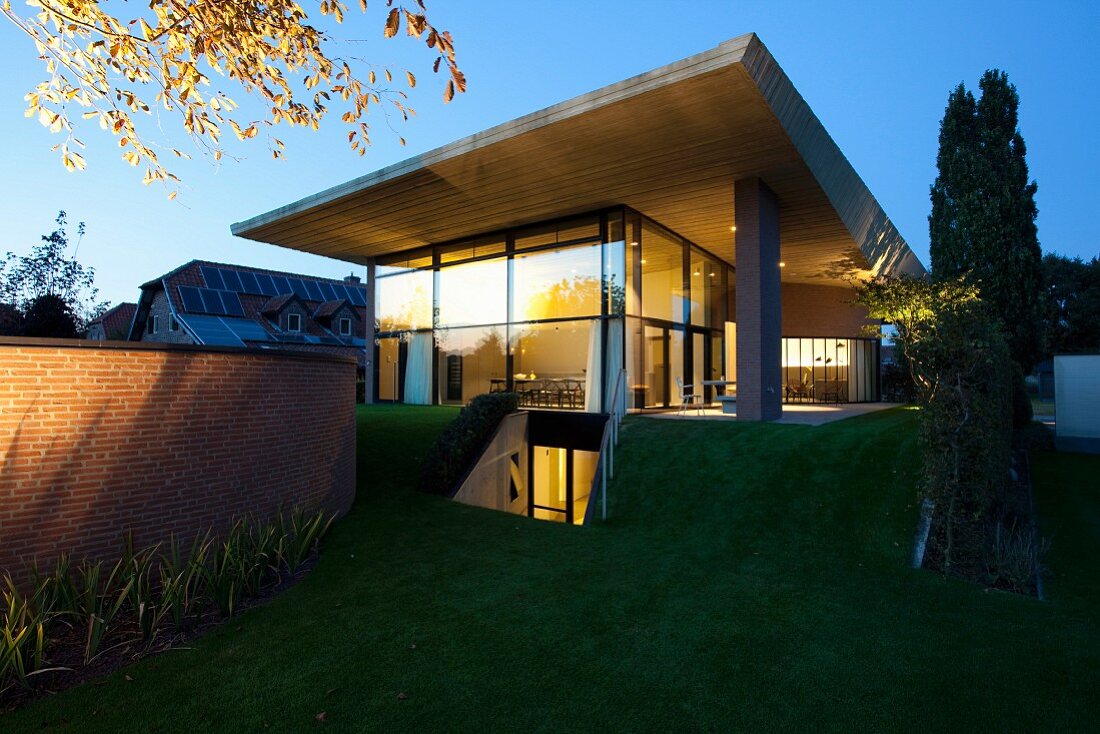 Contemporary house with protruding concrete roof at twilight with illuminated interior