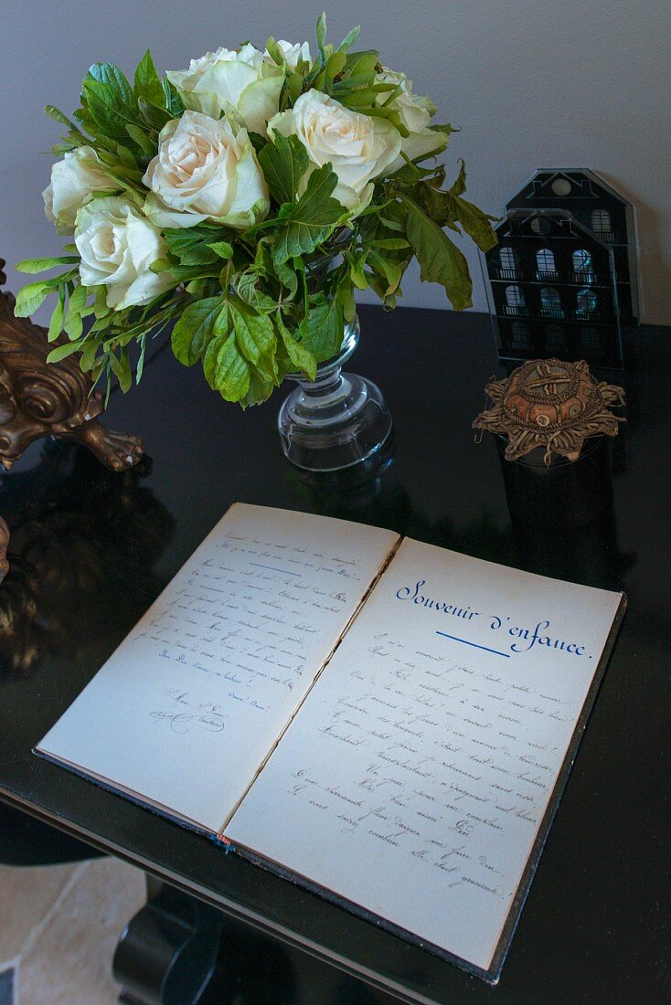 Aufgeschlagenes Tagebuch vor weißem Rosenstrauss in Glasvase