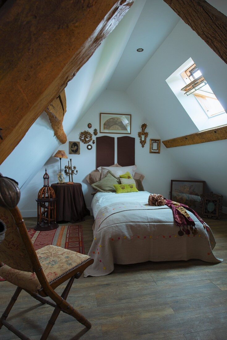 Bett in ausgebautem Spitzboden mit rustikaler Holzkonstruktion, im Vordergrund antiker Klappstuhl