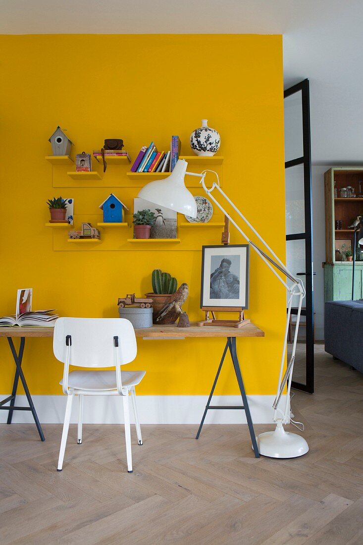 Tischplatte auf Metallböcken vor gelber Wand und weiss lackierter Retro Stuhl, seitlich moderne Stehleuchte