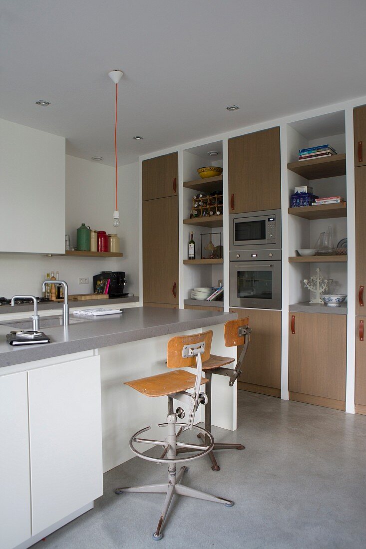 Kücheninsel, drehbare Retro Barhocker, oberhalb minimalistische Pendelleuchte mit Glühbirne in moderner, offener Küche