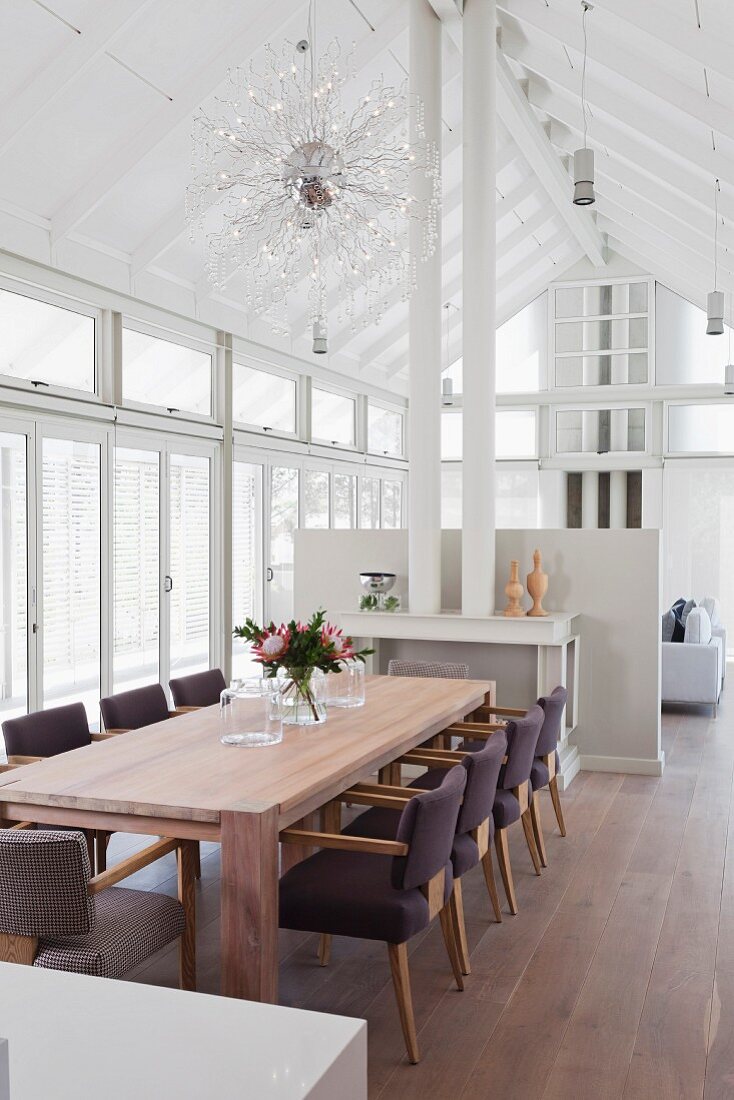 Dining area with upholstered chairs around wooden table in front of stove pipes and half-height partition wall in modern, white interior