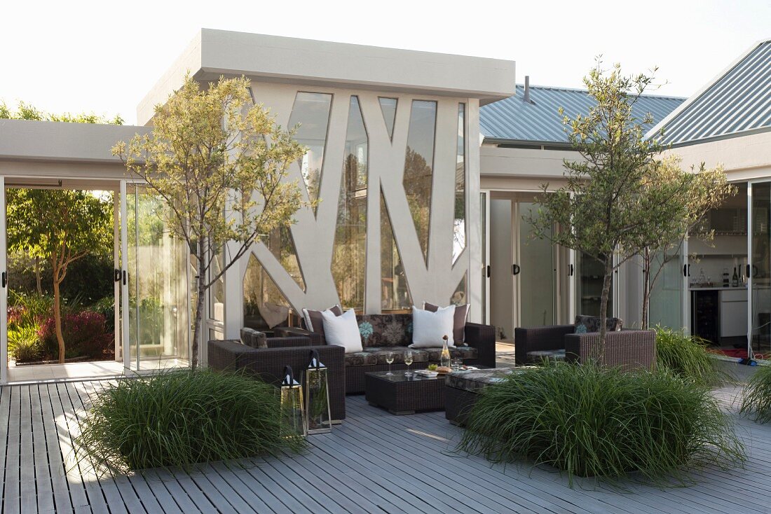 Trees in large planters and modern, dark wicker outdoor furniture on terrace in front of steel and glass façade