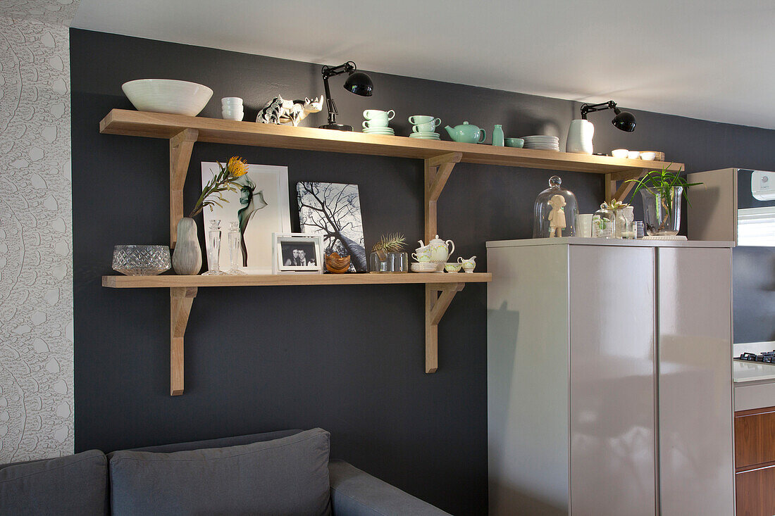 Crockery on wooden bracket shelves above pale grey cabinet against dark grey wall