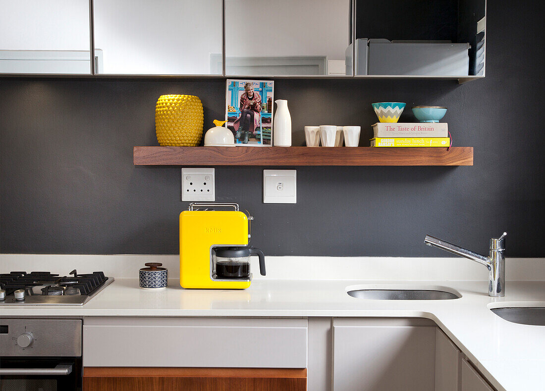 White kitchen worksurface with two integrated sinks and yellow coffee machine against dark grey wall