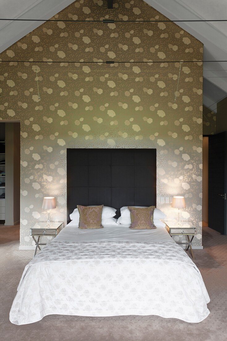 Double bed with dark headboard against wall with floral pattern