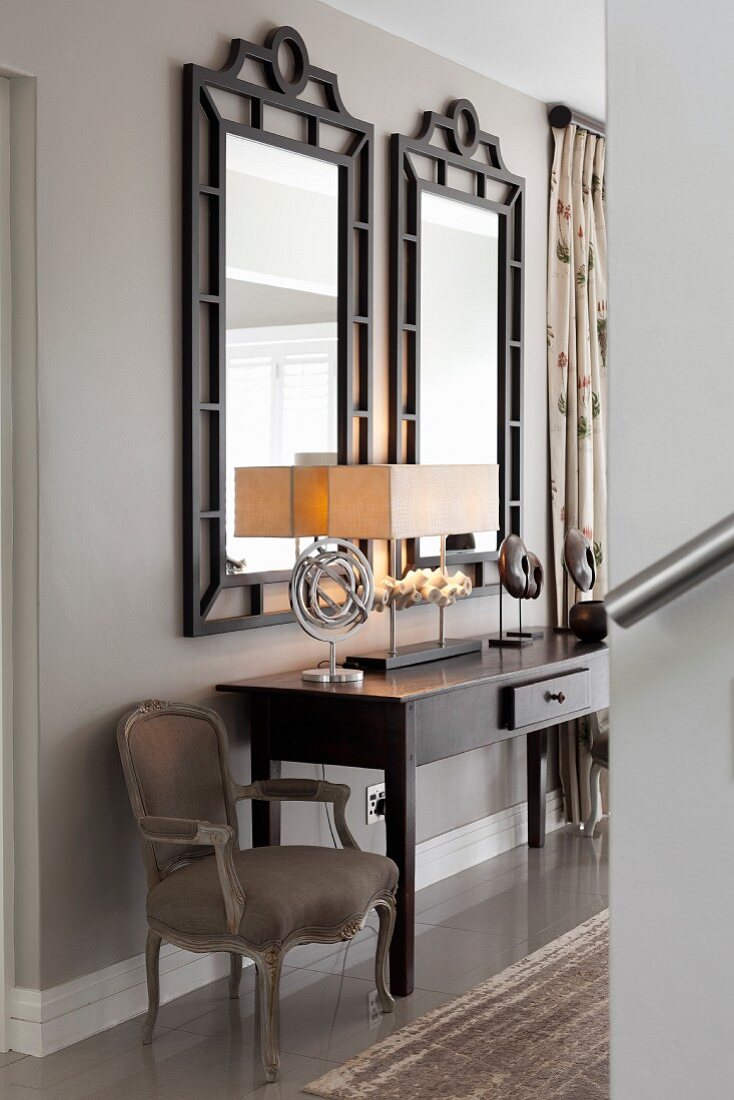 Dunkler Konsoltisch in einer eleganten Diele mit barockem Sessel und zwei schwarz gerahmten Spiegeln