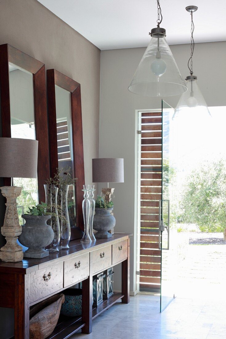 Wood-framed mirrors, urns and table lamps on Colonial-style sideboard and pendant lamps with glass lampshades