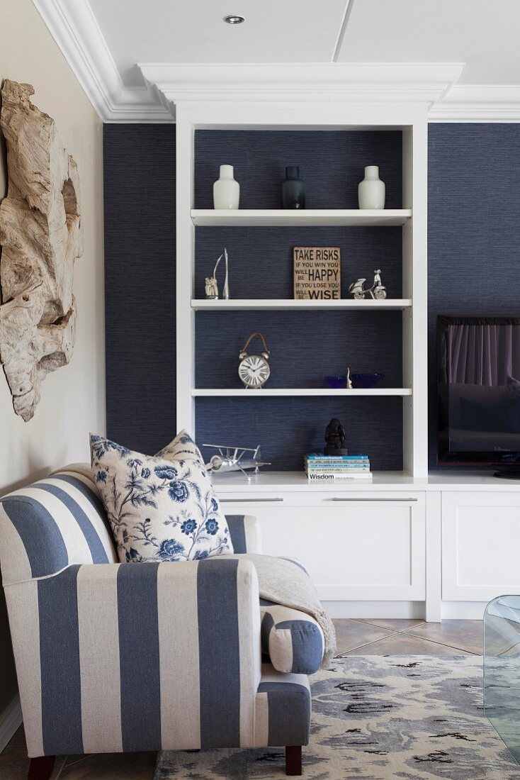 White, fitted shelving against dark blue wallpaper in living room