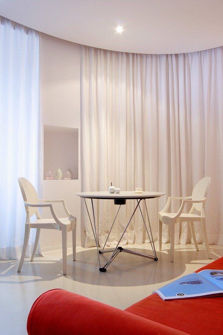 weiße Ghost Stühle an Tisch vor weißem Vorhang als Raumteiler, im Vordergrund orangefarbenes Polstersofa
