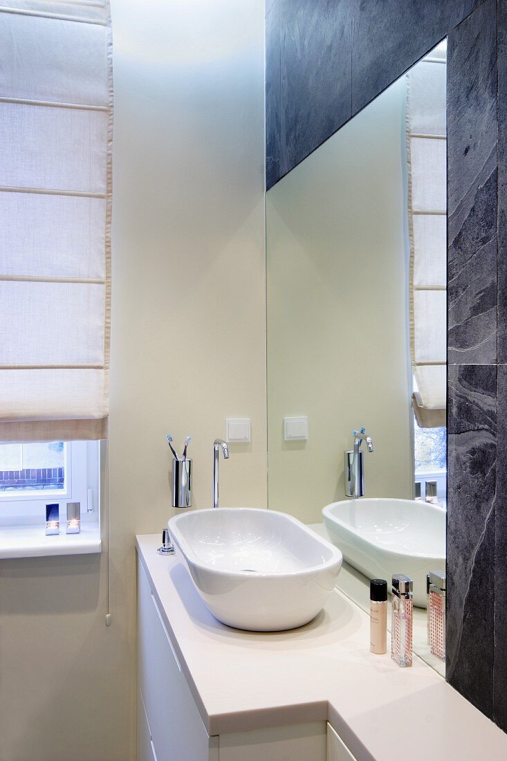 Washbasin on base unit in front of mirror integrated in wall in corner of modern bathroom