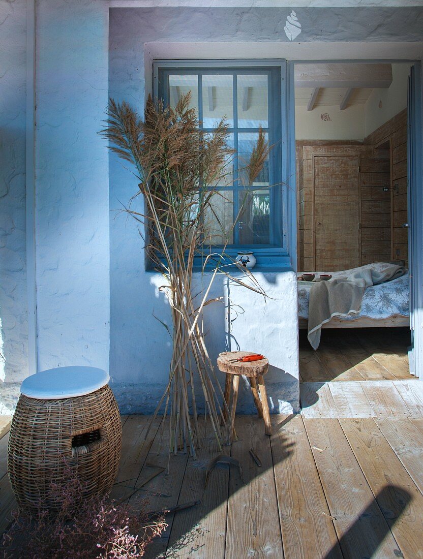 Rattan Hocker mit Sitzkissen und Pampasgras auf Holzterrasse mit Blick ins Schlafzimmer