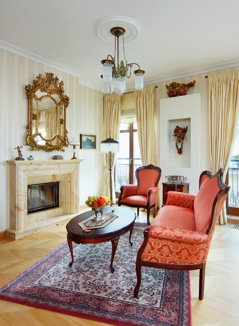 Baroque-style couch with red and gold ornate upholstery, antique coffee table and fireplace in corner of grand living room