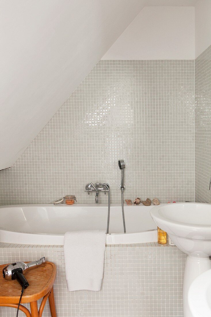 Small bathroom with white glass mosaic tiles under sloping ceiling