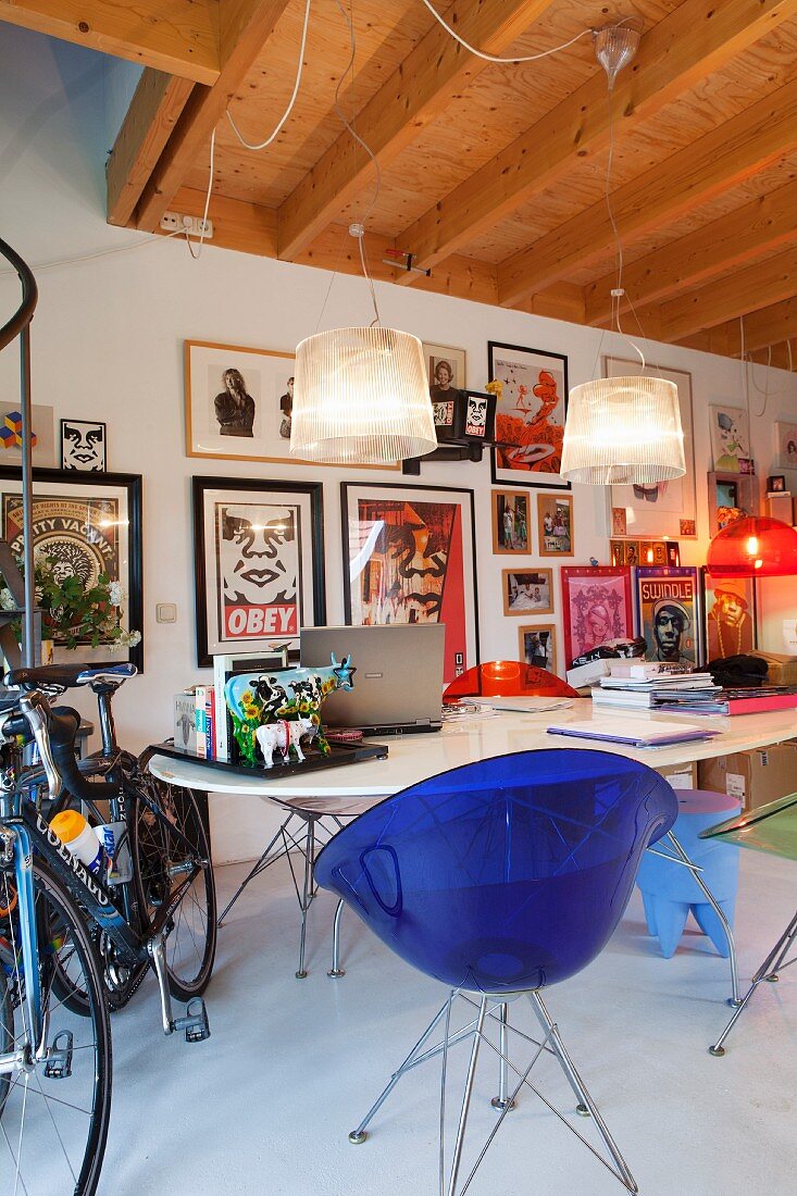 Retro Schalenstuhl aus blauem Kunststoff an Tisch, Bildersammlung an der Wand, seitlich Fahrräder
