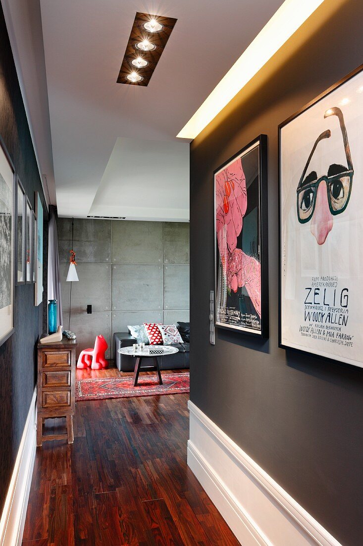 Schmaler Gangbereich mit schwarzen Wänden und Plakat, Blick in Loungeecke vor Betonwand