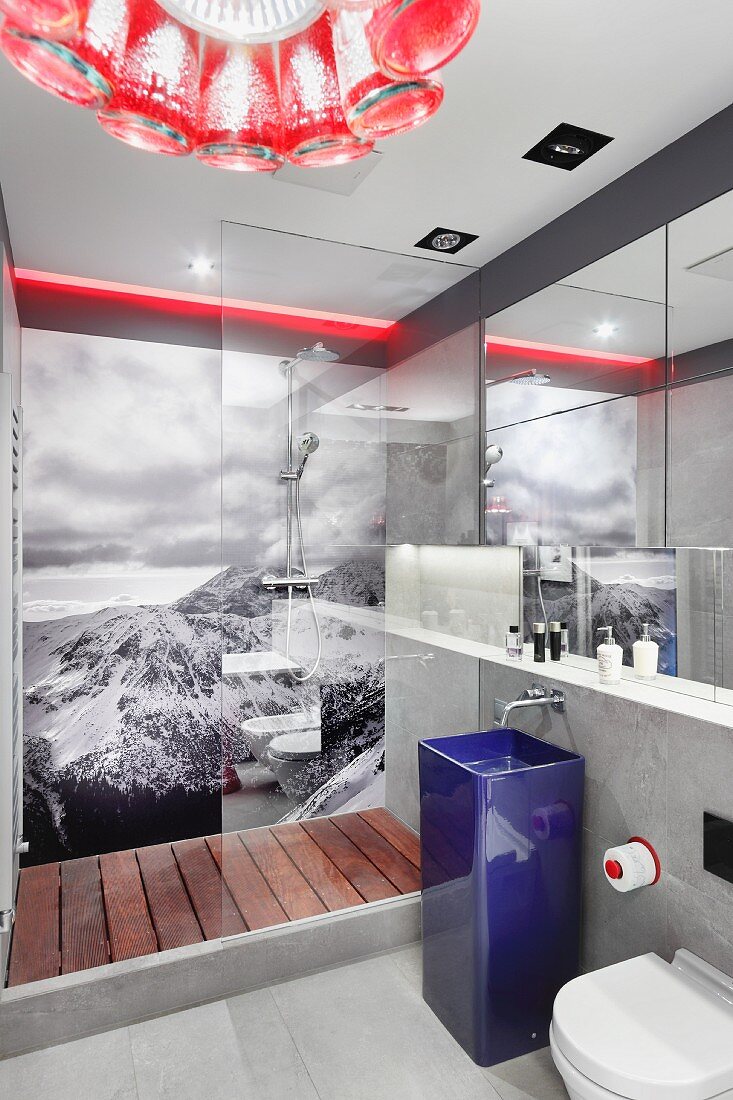 Designer bathroom with blue pedestal sink in front of glazed shower area with black and white photo mural