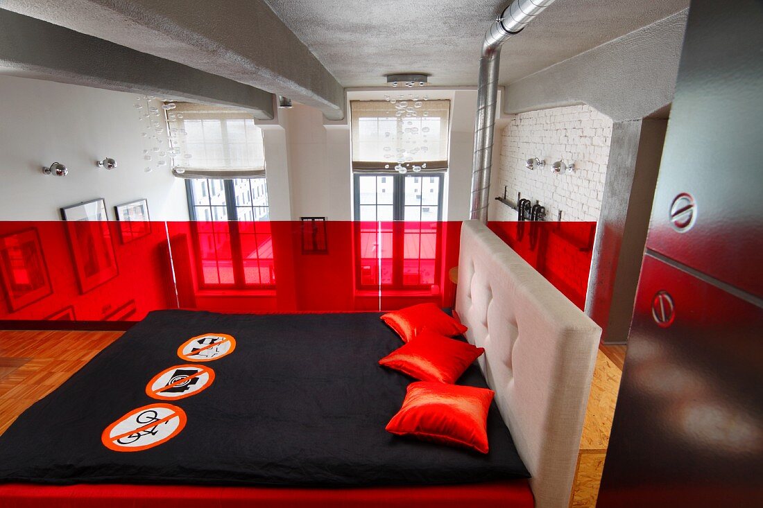 Schlafbereich auf Galerie, Doppelbett mit schwarzer Tagesdecke und roten Kissen vor roter Glasbrüstung