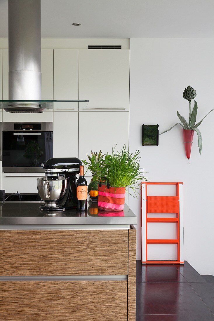 Einbauküche mit Küchenblock und Edelstahlarbeitsplatte, orangefarbene Trittleiter an weißer Wand