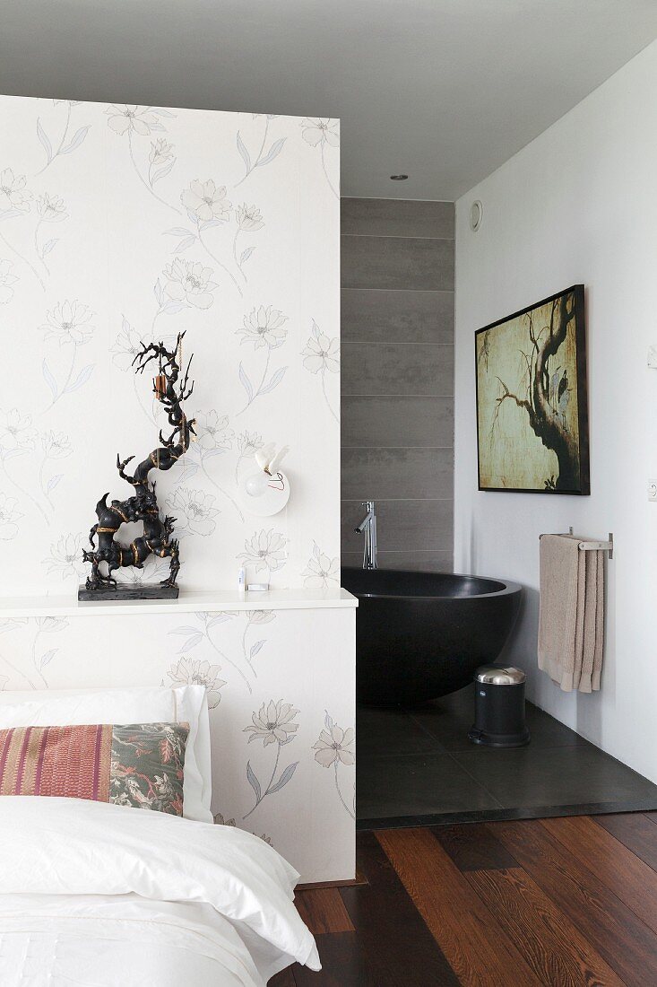 Subtle floral wallpaper on partition with ethnic sculpture on shelf and view of free-standing bathtub in ensuite bathroom