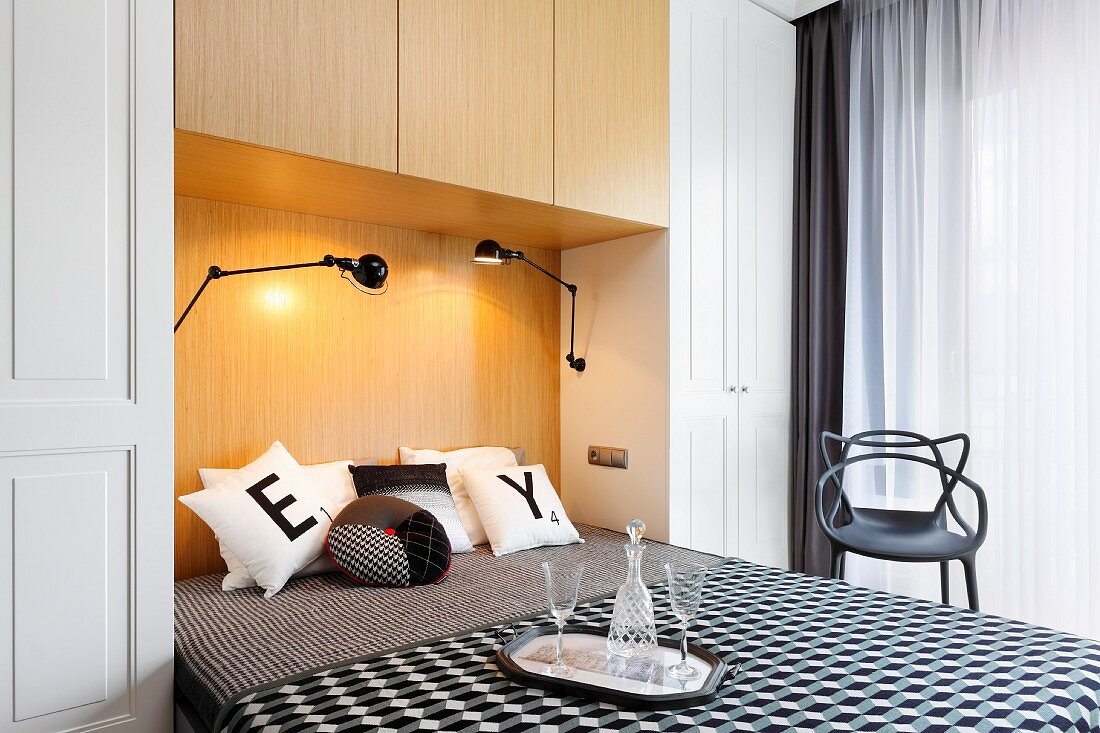In Schrankwand integriertes Doppelbett mit schwarz-weiss gemusterten Auflagen und Kissen, Tablett mit Gläsern und Karaffe