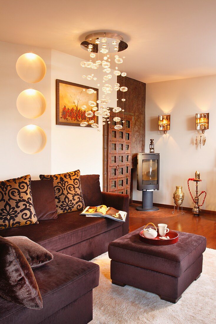 Pendant lamp with glass bubbles above dark brown corner sofa with matching ottoman; elegant interior with ethnic elements
