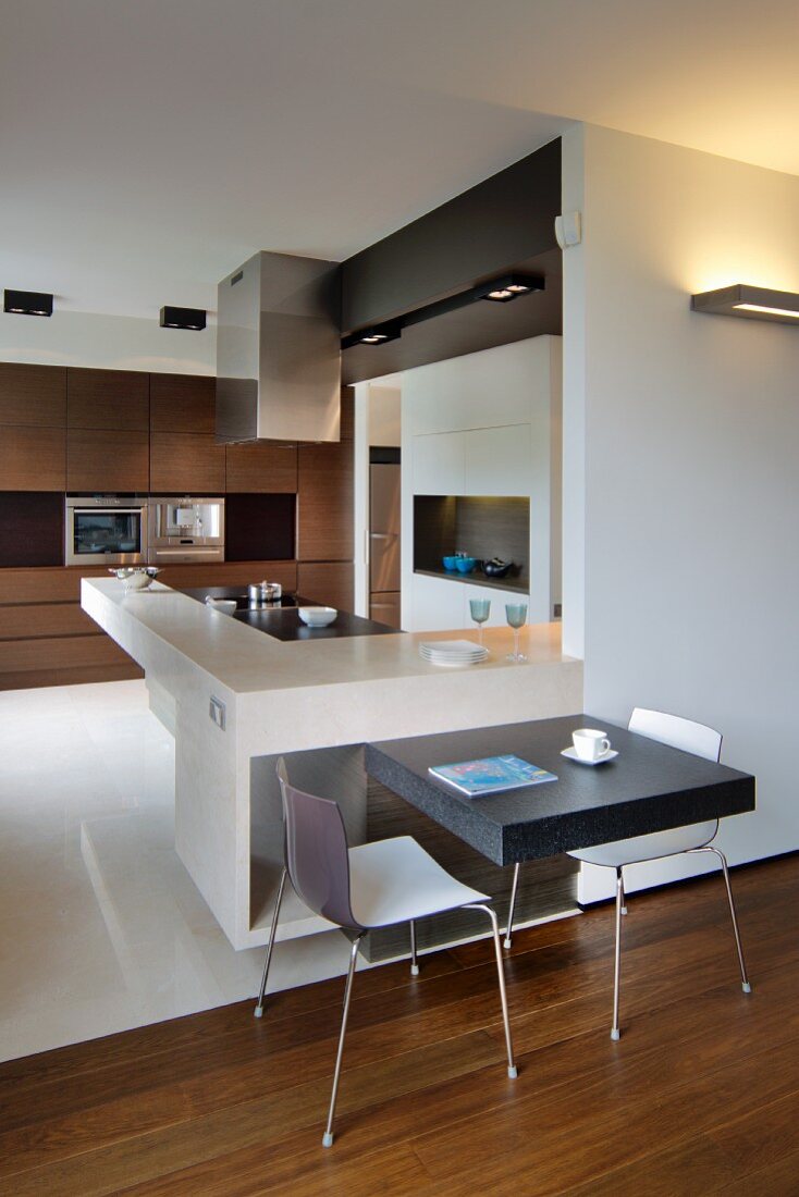 L-shaped kitchen counters with breakfast bar and integrated table for two; fitted cupboards with dark wooden fronts in background
