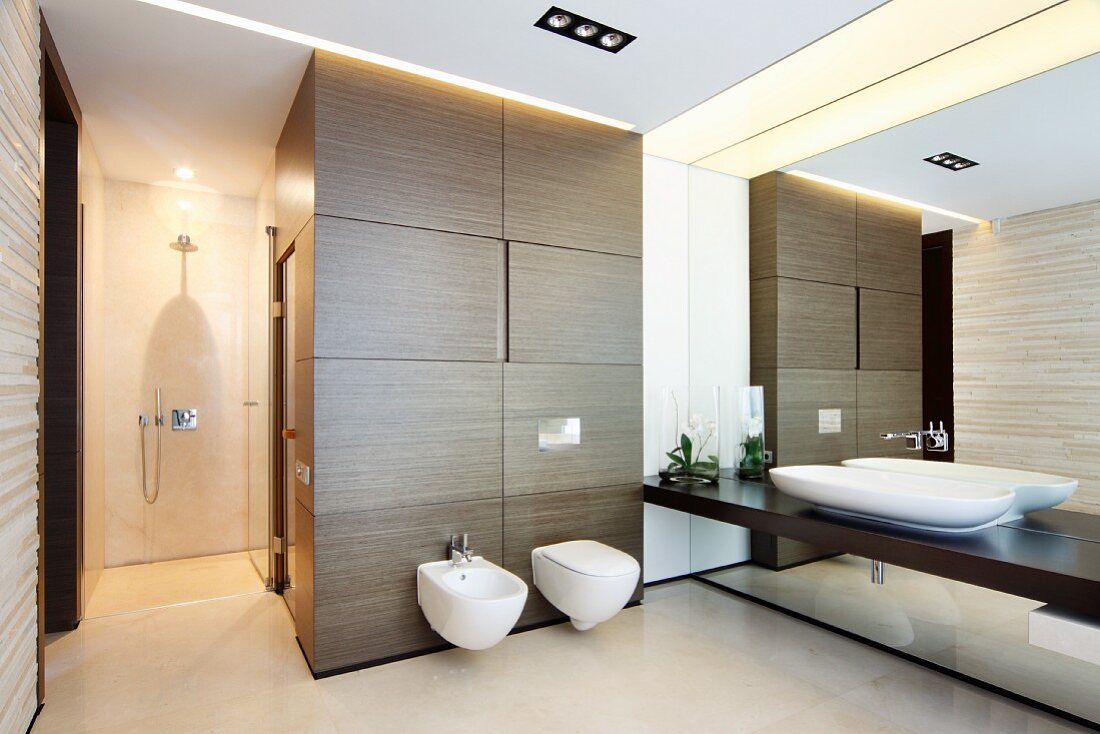 Designer bathroom with continuous washstand counter on mirrored wall, toilet and bidet on wood-clad sauna element and walk-in shower